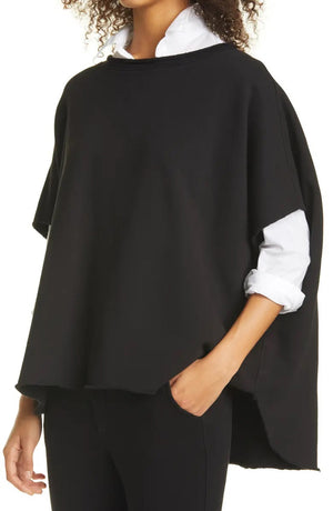 The FRANK & EILEEN OLIVE ORIGINAL CAPELET in black, by FRANK & EILEEN, is a black oversized T-shirt with a round neckline and short, wide sleeves. Made from 100% cotton, it features a loose fit and simple design reminiscent of a capelet against a light textured background.