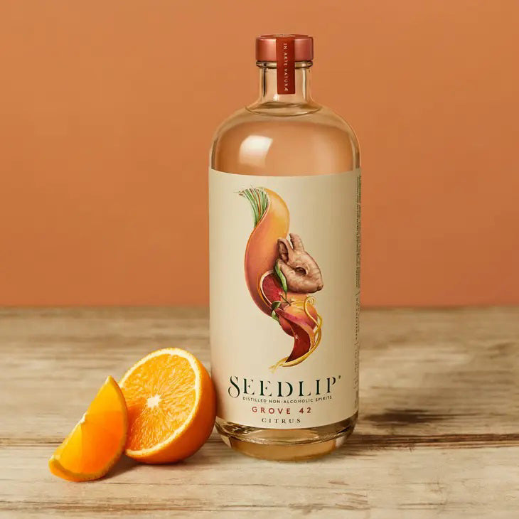 A glass bottle of SEEDLIP - GROVE 42 NON ALCOHOLIC SPIRITS from SEEDLIP DRINKS. The label, marked &quot;Grove 42 Citrus,&quot; features a colorful, artistic depiction of citrus fruits and leaves. This citrus blend is sealed with a red cap, showcasing the clear liquid inside—a perfect choice among non-alcoholic options.