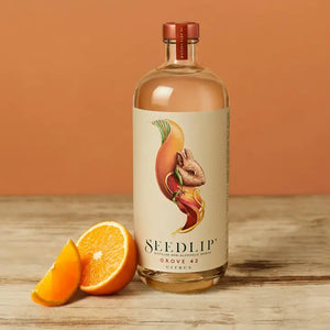 A glass bottle of SEEDLIP - GROVE 42 NON ALCOHOLIC SPIRITS from SEEDLIP DRINKS. The label, marked "Grove 42 Citrus," features a colorful, artistic depiction of citrus fruits and leaves. This citrus blend is sealed with a red cap, showcasing the clear liquid inside—a perfect choice among non-alcoholic options.