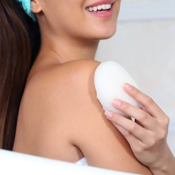 A white, teardrop-shaped Daily Concepts Konjac Sponge - Pure is displayed next to its transparent, branded packaging. The packaging emphasizes its eco-friendly and vegan features, along with its 100% natural and preservative-free Konjac root composition for a gentle skin cleanse inspired by Japanese beauty traditions.