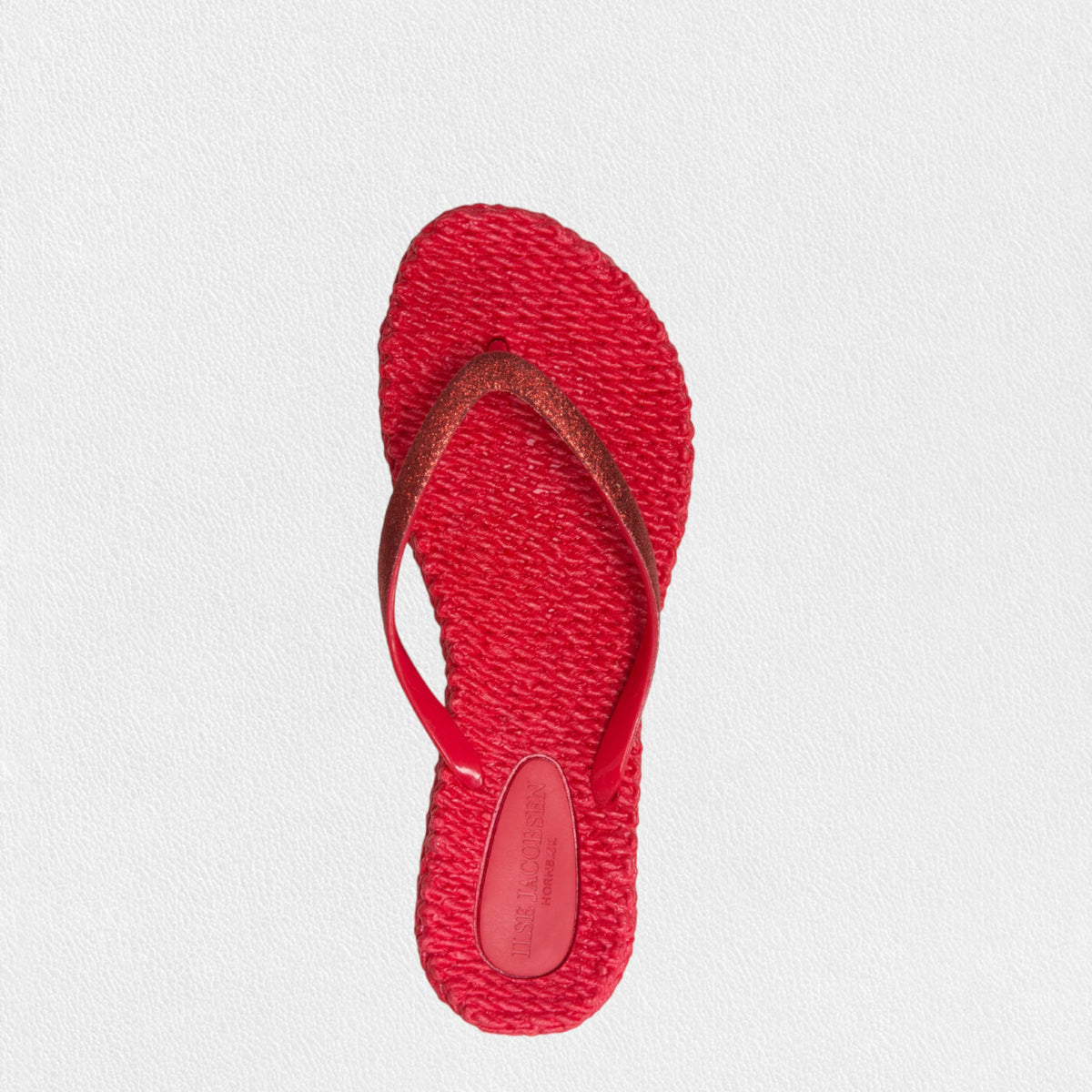 The ILSE JACOBSEN CHEERFUL FLIP FLOP IN DEEP RED by LINES OF DENMARK features vibrant red sandals with textured soles, glitter straps, and a comfortable fit, elegantly placed on a plain white surface.