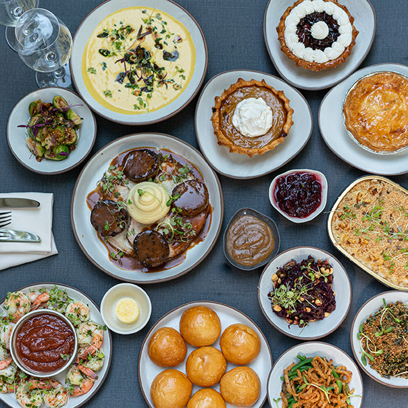 A Thanksgiving Takeout for Two spread on a table at Fearrington Barn, including bowls of soup, roasted meat with mashed potatoes, side dishes, rolls, and small pies.