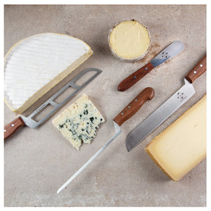 A selection of three professional cheese knives from FORMATICUM's KNIFE GIFT S4, handmade in Italy with stainless steel blades, is beautifully arranged on a stone surface alongside various cheeses. The assortment includes a large wedge of brie, a round of Camembert, blue cheese, and hard cheese. The knives feature wooden handles and are thoughtfully placed near their respective cheeses.