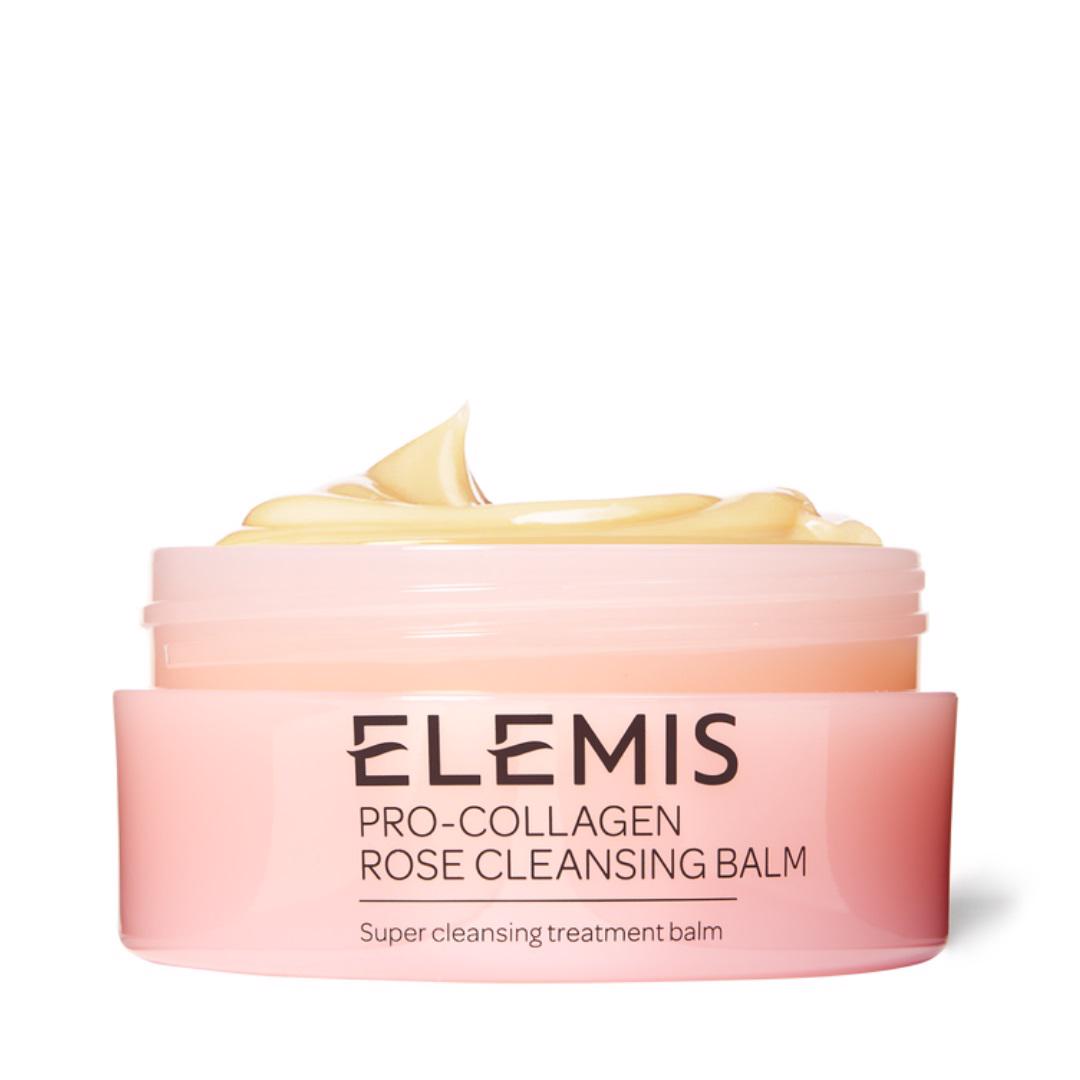 An open container of ELEMIS Pro-Collagen Cleansing Balm, infused with English Rose Oleo Extract, reveals a visible swirl of light yellow product on top. The pink and white container is labeled with the product name and &quot;ELEMIS - STEINER,&quot; indicating it is a &quot;super cleansing treatment balm&quot; ideal for sensitive skin.