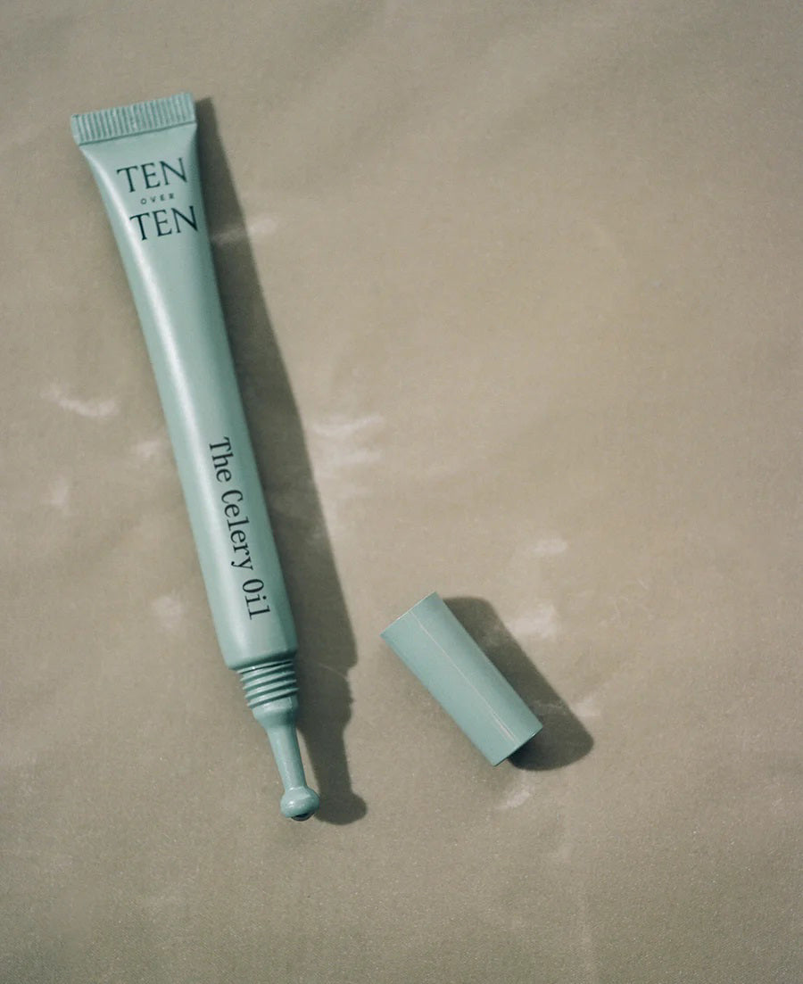 A light blue tube labeled "TENOVERTEN - THE CELERY OIL" by TEN OVER TEN, known for its nourishing nail treatment and repair benefits, rests uncapped on a beige surface.