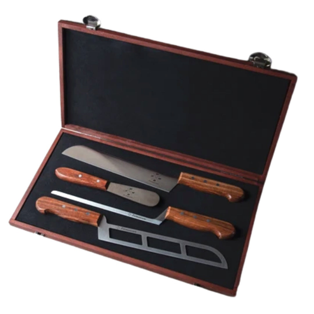 A selection of three professional cheese knives from FORMATICUM&#39;s KNIFE GIFT S4, handmade in Italy with stainless steel blades, is beautifully arranged on a stone surface alongside various cheeses. The assortment includes a large wedge of brie, a round of Camembert, blue cheese, and hard cheese. The knives feature wooden handles and are thoughtfully placed near their respective cheeses.