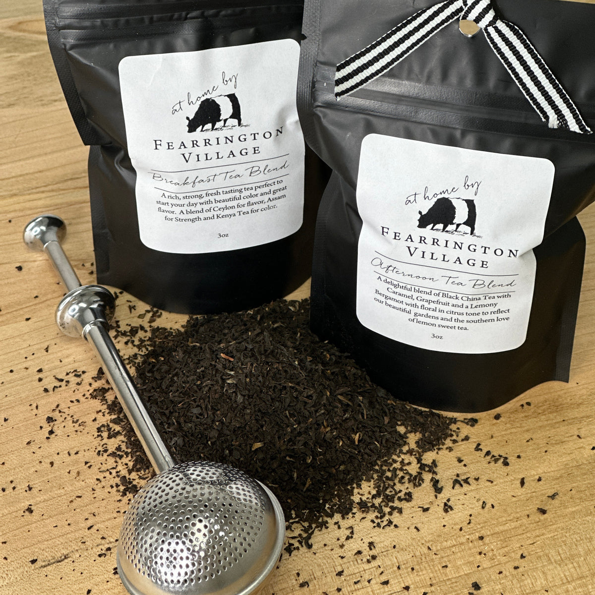 A black resealable bag of the Fearrington Signature Collection - Fearrington Signature Breakfast Tea Blend. The white label prominently displays the Fearrington House brand and describes it as &quot;An elegant blend of Ceylon and Assam with a hint of Keemun for strength.&quot; This loose leaf tea is adorned with a striped ribbon on top, offering a rich, strong tea experience.