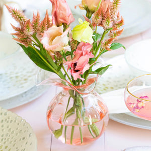 The VIETRI Hibiscus Bud Vase Pink features clear glass with a pale pink tint and a wide, wavy flared rim, inspired by Tuscan artisan craftsmanship and Hibiscus glass designs. Set against a white background.