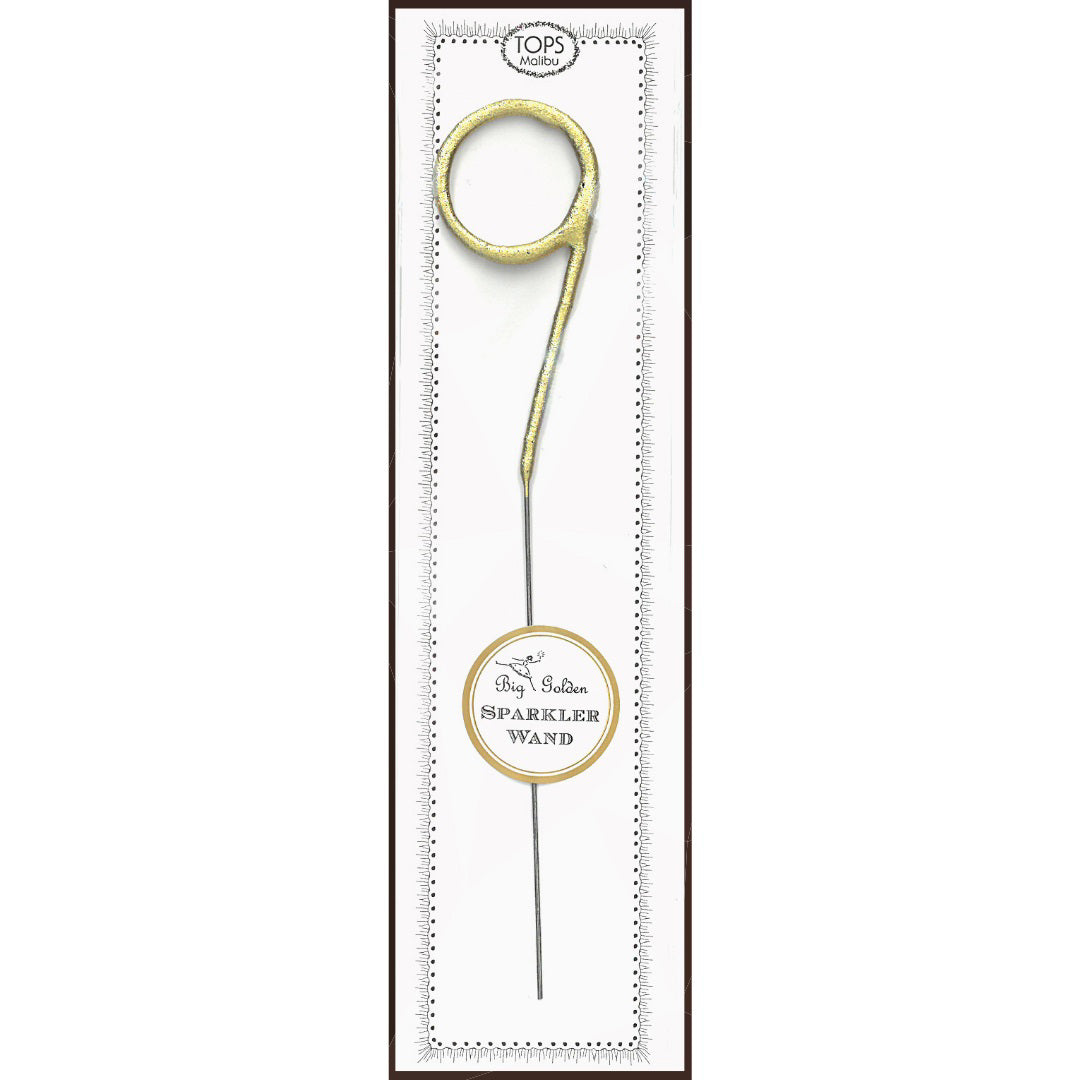 A "WAND BIG GOLD SPARKLER 9" from TOPS MALIBU, perfect as a cake topper, is displayed inside a white and black rectangular packaging with a transparent window. The top of the packaging reads "TOPS Malibu," while the bottom section features a round label with the text "Big Golden Sparkler Wand.