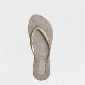 The ILSE JACOBSEN - CHEERFUL FLIP FLOPS IN ATMOSPHERE from LINES OF DENMARK are designed with beige straps adorned with golden glitter and glitter stones, set against a simple, light-colored background. They feature a textured sole that resembles a woven pattern, enhancing their casual, summery vibe and ensuring a comfortable fit for any party occasion.
