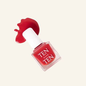 A glass bottle of TENOVERTEN - NAIL POLISH from the brand TEN OVER TEN, featuring a white cap and a dusty pink nail color. The front label displays "TEN OVER TEN" in white uppercase letters. This vegan, eight-free formula ensures both beauty and peace of mind. The background is plain and light-colored.
