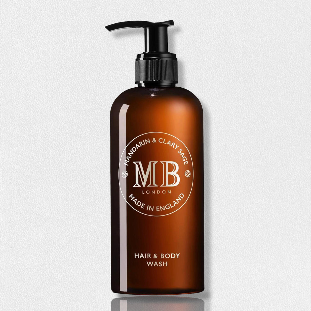 Amber-colored bottle with a black pump dispenser labeled &quot;Mandarin &amp; Clary Sage, Molton Brown, Made in England&quot; with &quot;Hair &amp; Body Wash&quot; at the bottom. Infused with mandarin extract, this versatile FEARRINGTON LIFESTYLE COLLECTION - MOLTON BROWN 1971 COLLECTION MANDARIN CLARY SAGE HAIR &amp; BODY WASH is placed against a plain white background.