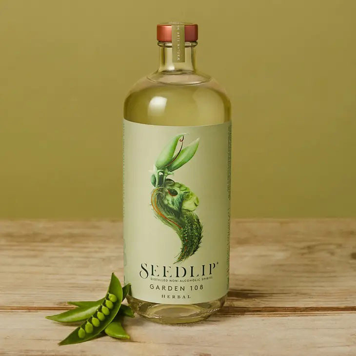 A clear glass bottle of SEEDLIP - GARDEN 108 NON ALCOHOLIC SPIRIT by SEEDLIP DRINKS, featuring a copper cap and a green and beige plant-themed label, showcases its refreshing herbal blend among non-alcoholic options.