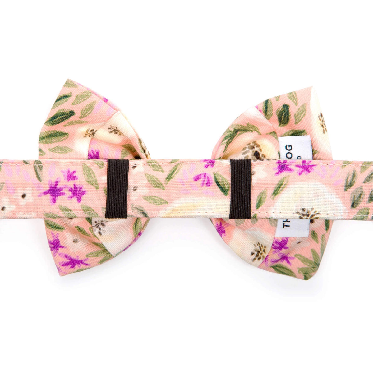 The Foggy Dog&#39;s standard Harper Floral dog bow tie features a pink base adorned with green leaves, ivory and purple flowers, and small black dots. The soft-textured fabric along with its delicate color palette evokes a spring-like feel.