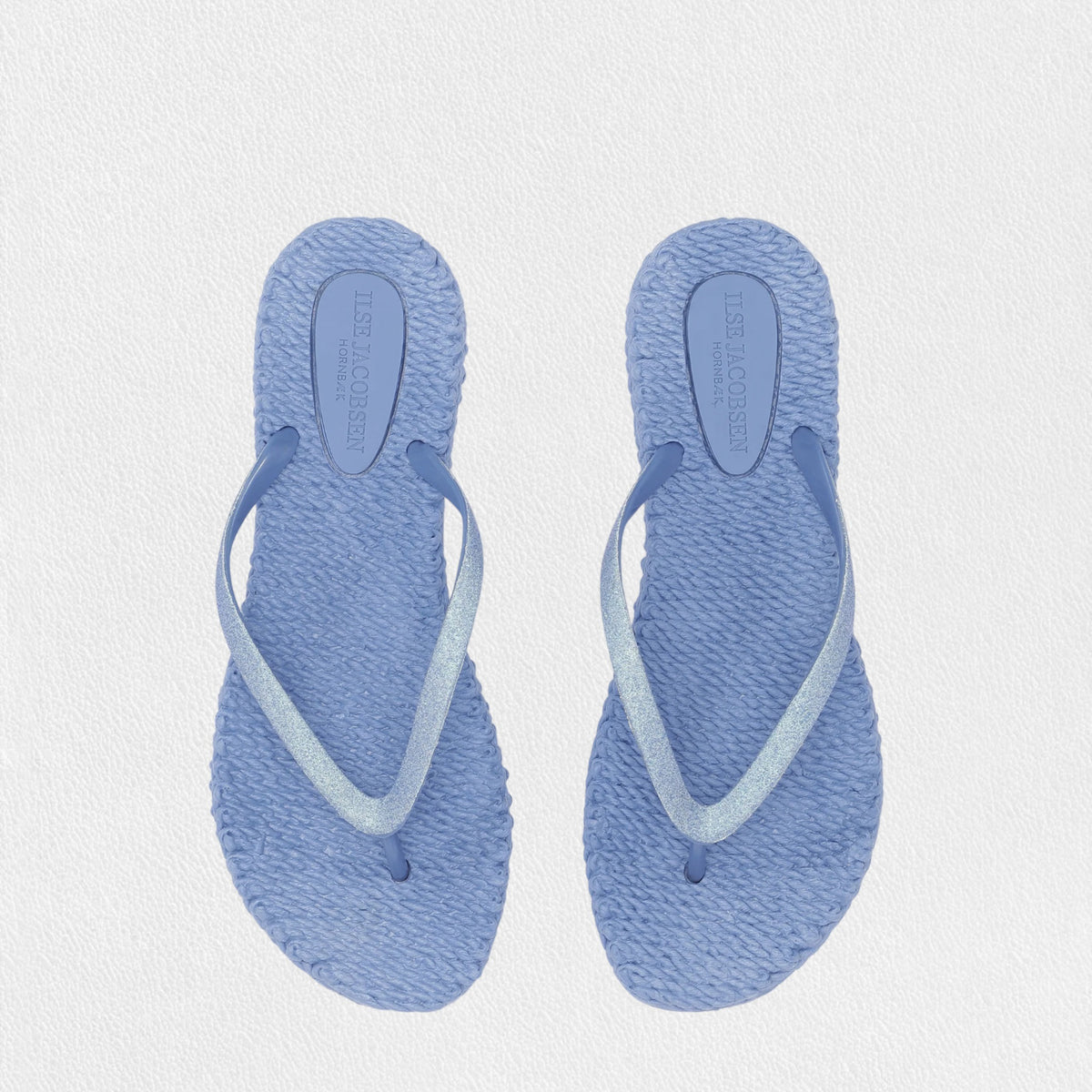 Introducing the ILSE JACOBSEN - CHEERFUL SLIPPER IN LIGHT REGATTA by LINES OF DENMARK, a pair of light blue flip-flops featuring woven straw soles and simple straps. These lightweight flip-flops, showcased against a plain white background, exude a minimalistic and casual style while ensuring a comfortable fit.
