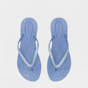 Introducing the ILSE JACOBSEN - CHEERFUL SLIPPER IN LIGHT REGATTA by LINES OF DENMARK, a pair of light blue flip-flops featuring woven straw soles and simple straps. These lightweight flip-flops, showcased against a plain white background, exude a minimalistic and casual style while ensuring a comfortable fit.
