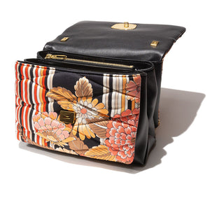 Introducing the VINATAGE SCARF AND LEATHER HANDBAG RED & BLACK by MILANO MM33. This stylish lambskin handbag boasts a colorful floral and striped pattern, reminiscent of a vintage scarf bag. The design includes vibrant shades of orange, red, black, and white. It features a quilted texture, a prominent buckle on the front, and a gold chain strap. Proudly made in Italy.