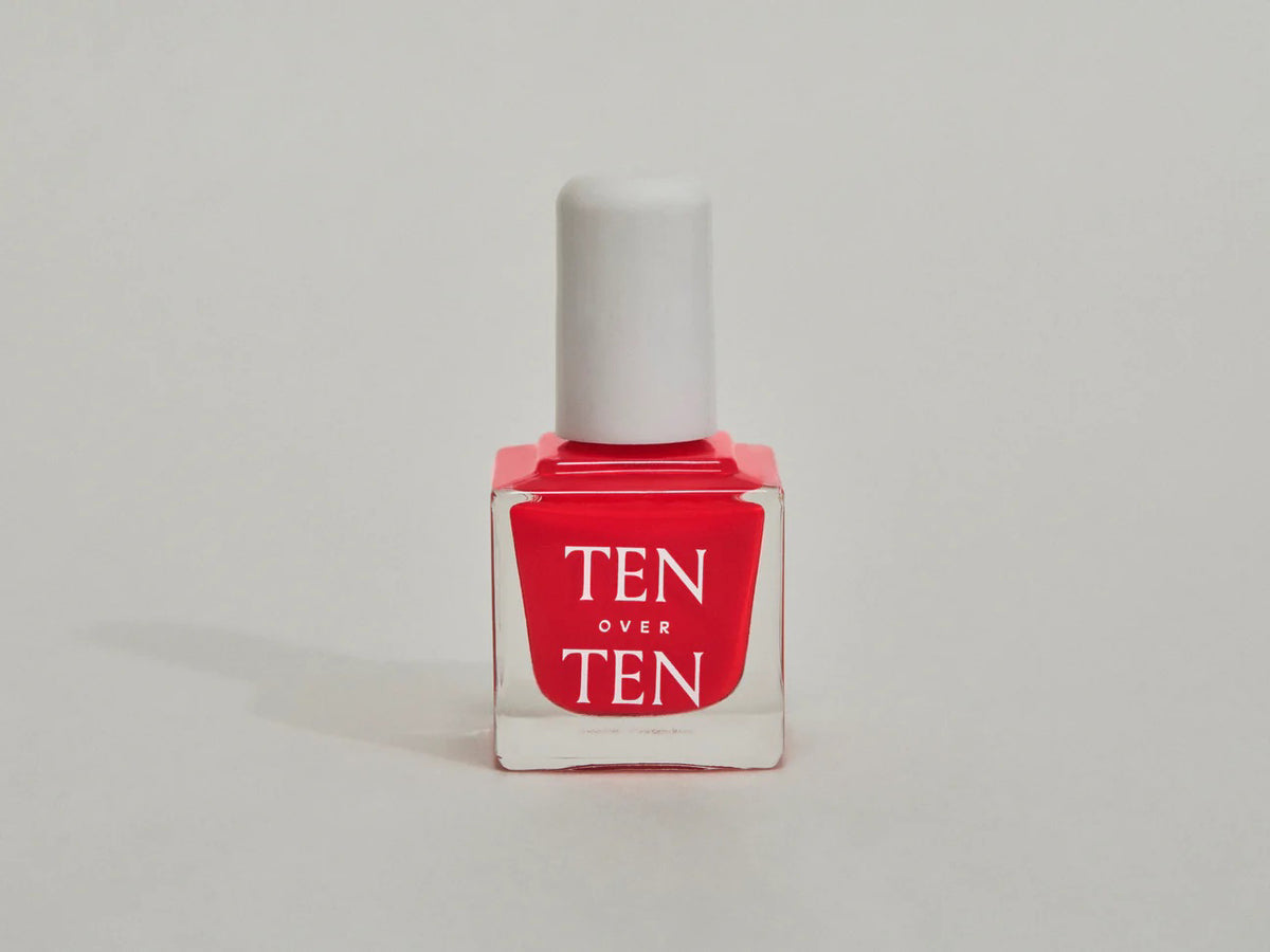 A glass bottle of TENOVERTEN - NAIL POLISH from the brand TEN OVER TEN, featuring a white cap and a dusty pink nail color. The front label displays "TEN OVER TEN" in white uppercase letters. This vegan, eight-free formula ensures both beauty and peace of mind. The background is plain and light-colored.