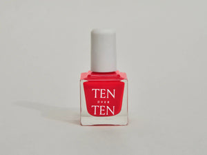 A glass bottle of TENOVERTEN - NAIL POLISH from the brand TEN OVER TEN, featuring a white cap and a dusty pink nail color. The front label displays "TEN OVER TEN" in white uppercase letters. This vegan, eight-free formula ensures both beauty and peace of mind. The background is plain and light-colored.