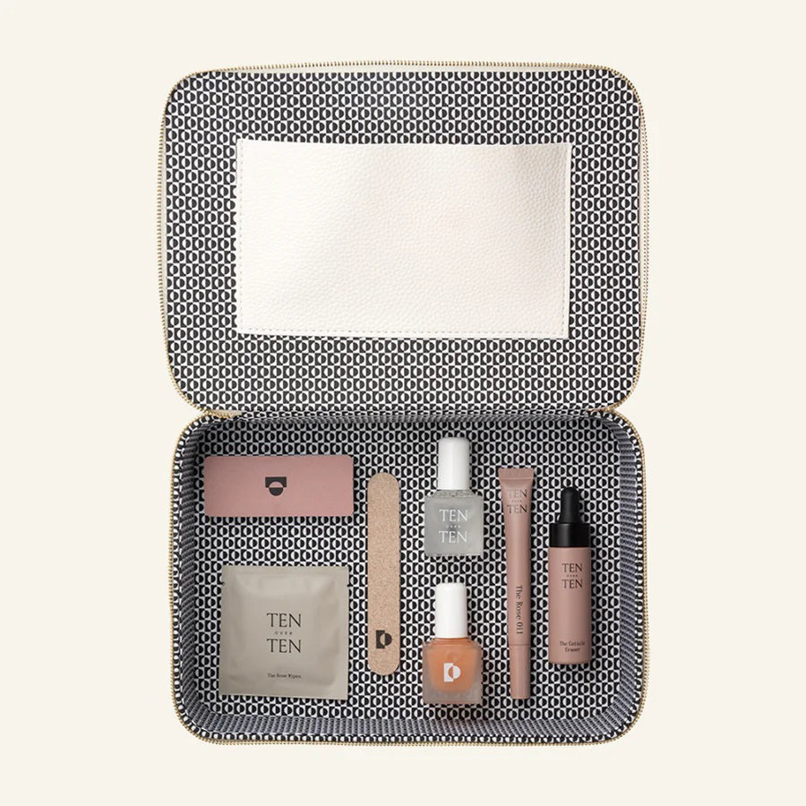 The TENOVERTEN - THE MANICURE KIT, by TEN OVER TEN, is showcased alongside various cosmetic items. The beige pouch features the text "TEN OUT OF TEN" and includes a Rose Oil dropper bottle, The Foundation, a cuticle eraser, a nail file, clear and white nail polish, a square bottle, a small box, and a tube.