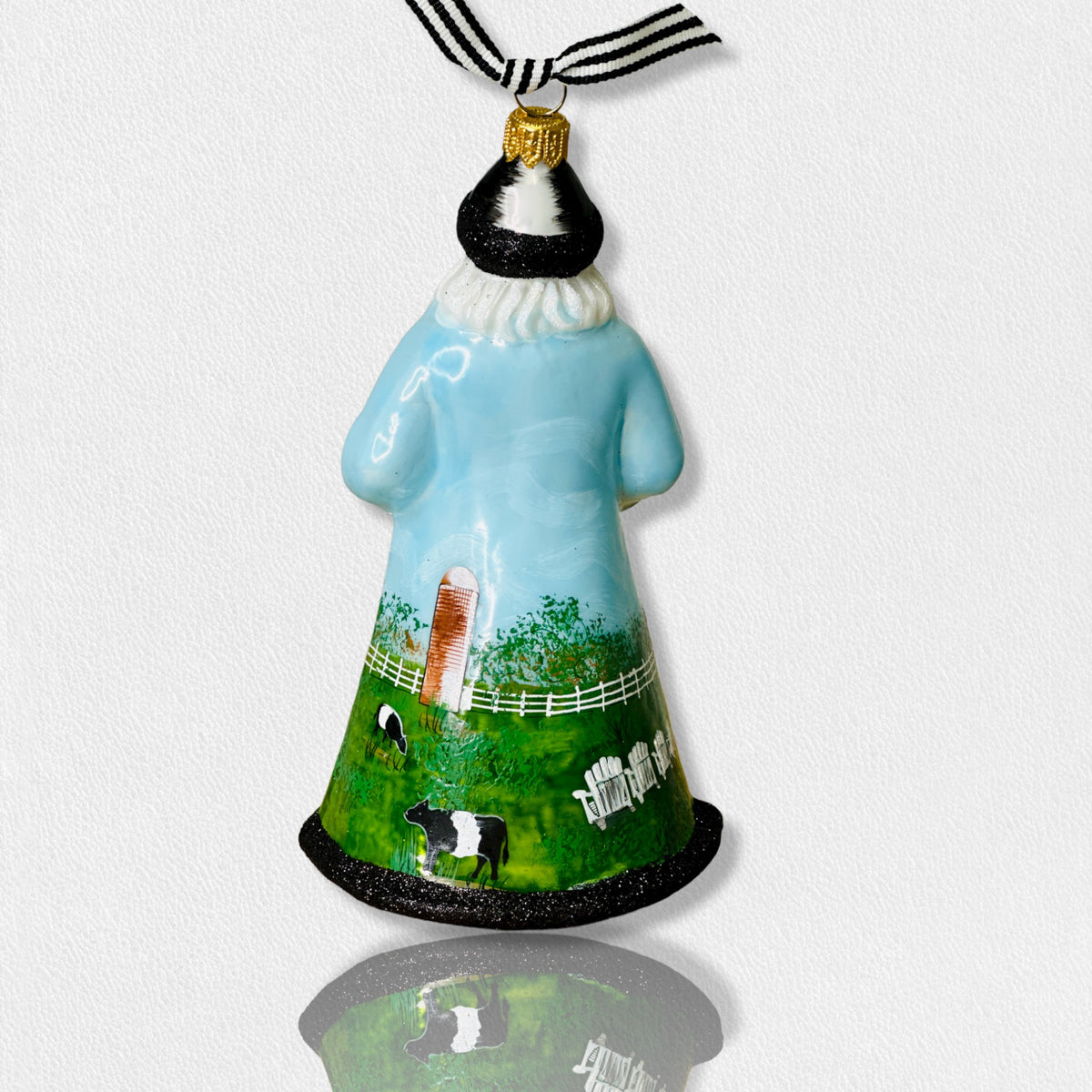 The Fearrington Signature Collection - Handmade Santa Ornament by Joy to the World Collectibles features a bearded figure in a blue robe adorned with farm scenes, including sheep, chickens, and a white fence. This hand-painted keepsake from Fearrington Village is topped with a gold cap and includes a black-and-white striped ribbon for hanging.