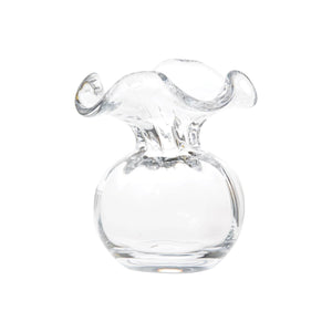 The VIETRI - HIBISCUS BUD VASE CLEAR by VIETRI features an artistic, wavy, and ruffled opening with a round base. This design resembles a blooming flower, crafted from smooth, transparent glass to showcase a modern and elegant aesthetic, making it perfect for any floral arrangement.