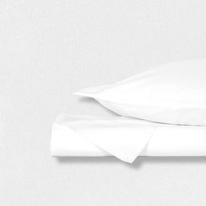 A neatly folded set of white cotton sateen pillowcases from the Fearrington Lifestyle Bedding Collection by Frette North America, boasting a luxurious 300 thread count, is tied with a black-and-white striped ribbon. Attached to the ribbon is a label featuring a small black silhouette of a person seated next to a large bear and the text "Fearrington." The background is light gray.