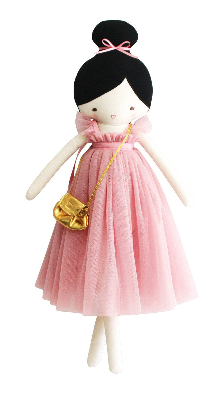 The ALIMROSE - CHARLOTTE DOLL BLUSH by ALIMROSE is a charming doll with black hair styled in a bun, dressed in a pink tulle dress with a high neckline and carrying a gold purse over her shoulder. Suitable for children aged 3 and up, the doll features simple embroidered facial details and a small, painted heart-shaped mouth.