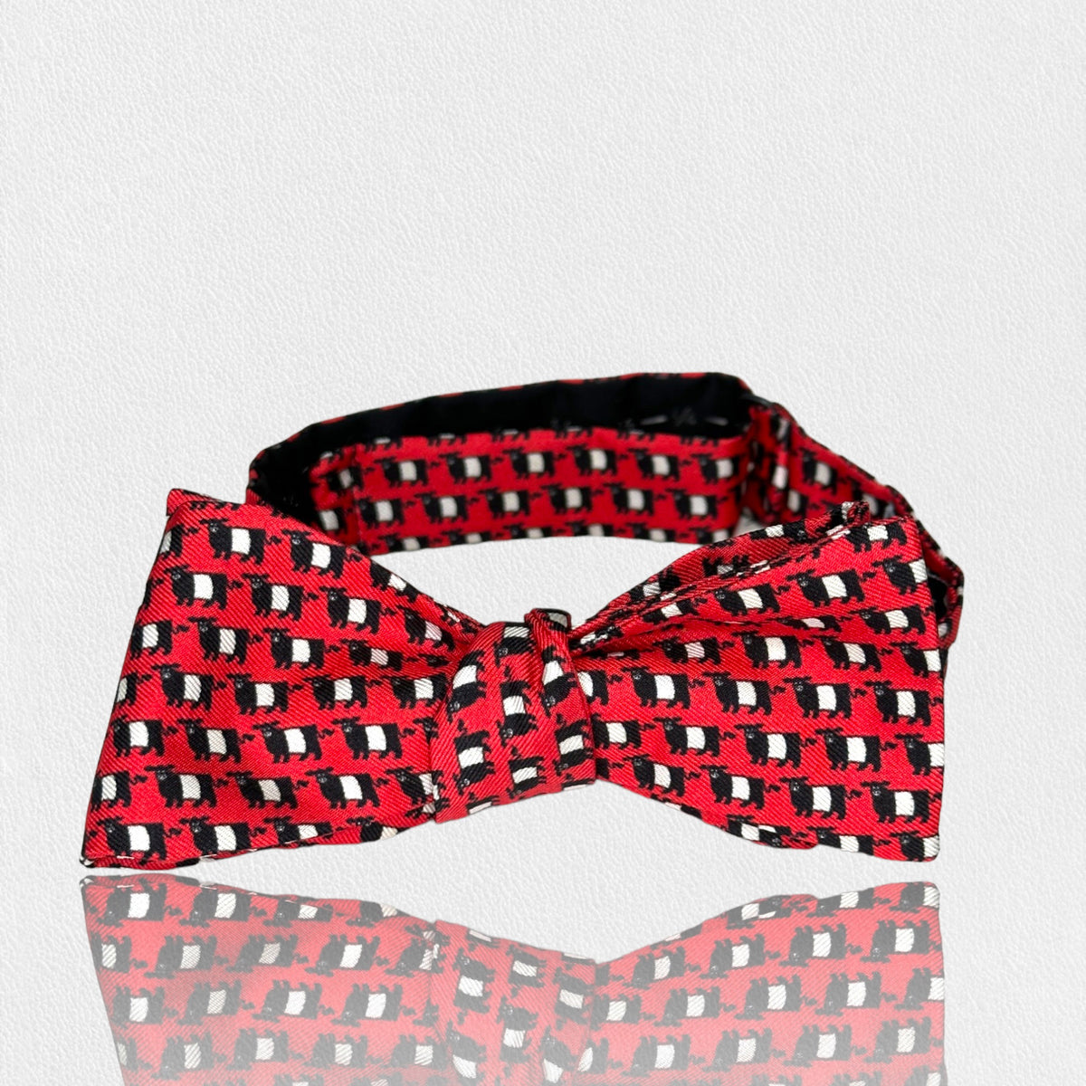 The FEARRINGTON SIGNATURE COLLECTION - BESPOKE BELTIE BOW TIE IN RED from COLLARED GREENS features a repeating pattern of small white and black rectangles on a white background. Made of handmade silk neckwear, the bow tie is neatly tied and presented in a frontal view, clearly displaying its intricate design.