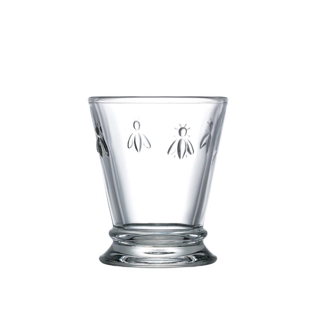 The BEE TUMBLER by LA ROCHERE is a clear glass tumbler with a slightly flared design, adorned with embossed insect motifs around the upper portion. This piece of durable glassware sits on a solid, slightly elevated base and is dishwasher safe.