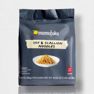 MOMOFUKU Soy and Scallion Noodles come in dark gray packaging with white and yellow accents, featuring a bowl of air-dried noodles on the front. Each pack highlights five servings, no preservatives, and restaurant-level flavor.