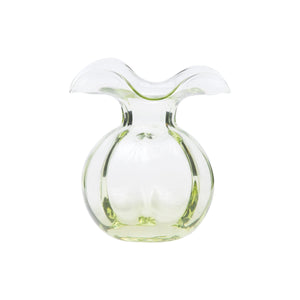 A clear, glass vase with a wide, ruffled opening and a slightly green-tinted round body. Created by Tuscan artisans, the VIETRI Hibiscus Bud Vase Green has a smooth, translucent surface and elegant curves, giving it a modern and artistic appearance.