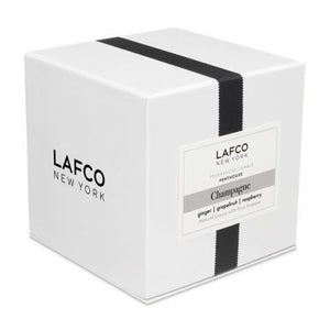 The LAFCO - CHAMPAGNE Penthouse 6.5oz candle holder by LAFCO is a small cylindrical piece featuring a frosted white exterior and a slightly transparent base. It casts a soft shadow to the right on a plain white background, evoking the refreshing essence of grapefruit.