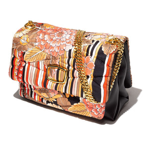 Introducing the VINATAGE SCARF AND LEATHER HANDBAG RED & BLACK by MILANO MM33. This stylish lambskin handbag boasts a colorful floral and striped pattern, reminiscent of a vintage scarf bag. The design includes vibrant shades of orange, red, black, and white. It features a quilted texture, a prominent buckle on the front, and a gold chain strap. Proudly made in Italy.