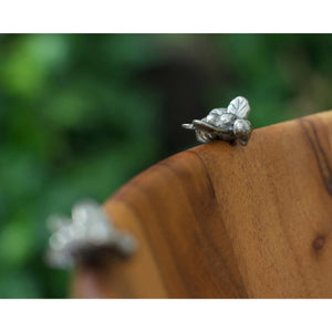 The VAGABOND HOUSE - BEE SALAD BOWL is a wooden serving dish with a ribbed design and pewter honeybee details on the rim. Made from acacia wood, it showcases a rich brown hue with natural grain patterns, enhancing any table setting elegantly.