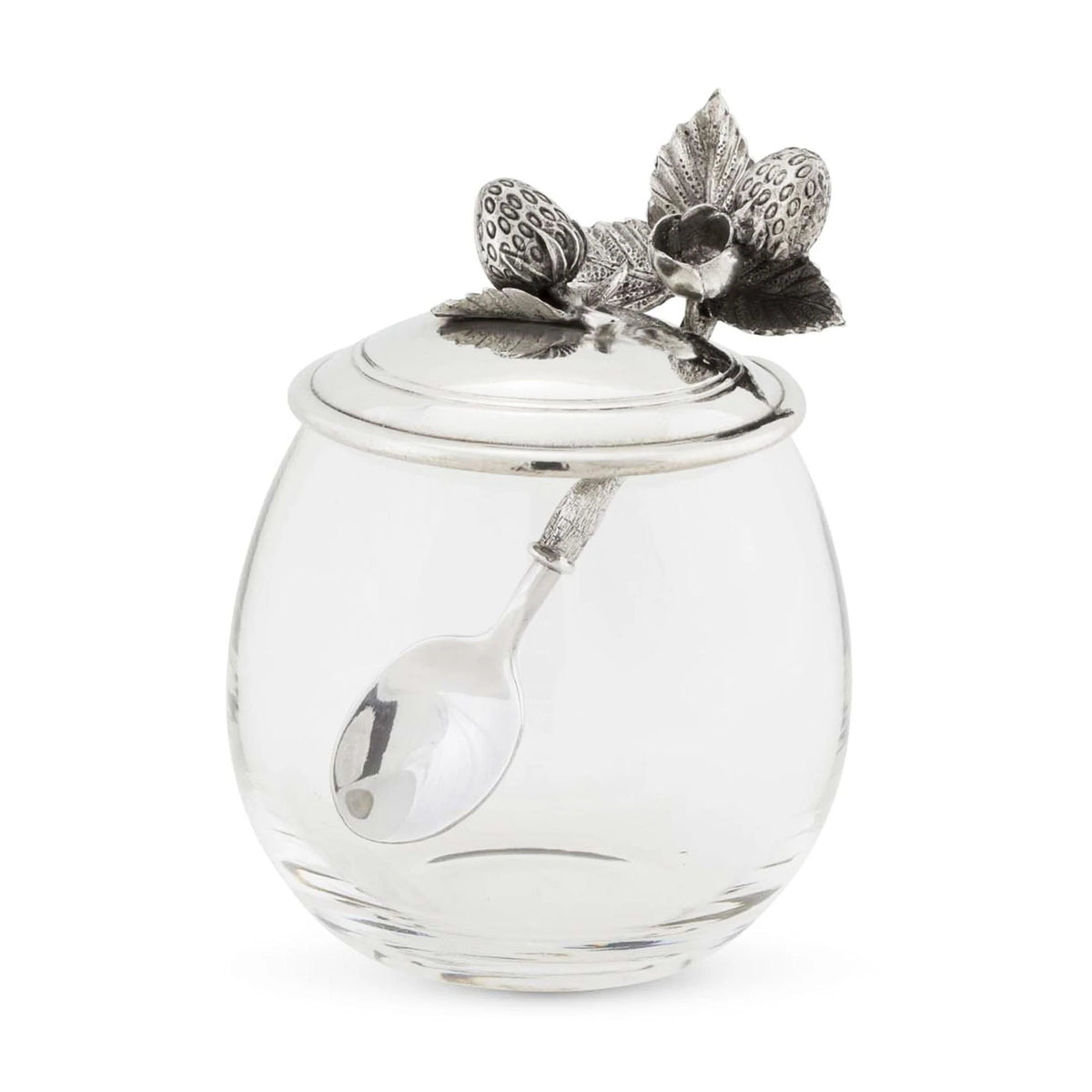 The VAGABOND HOUSE Strawberry Jam Jar features a silver lid with charming strawberry and leaf patterns. A small spoon from the set elegantly rests inside.