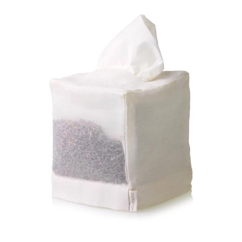 The LAVENDER SQUARE TISSUE COVER IVORY by E WIGHTMAN & CO is a neatly stitched white mesh cube filled with what appears to be dried lavender. A piece of thin white linen fabric protrudes from an opening at the top, and a small tag can be seen on the side.