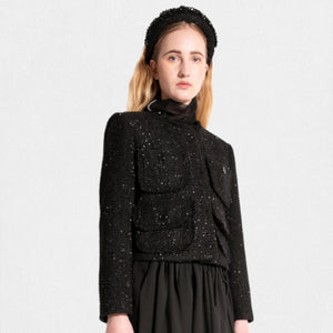 A woman with long blonde hair wears a MEIMEIJ LUREX TWEED JACKET by MEIMEIJ, which features front closure buttons and two large pockets on the chest. She has a black headband and a long black skirt. The background is plain off-white.