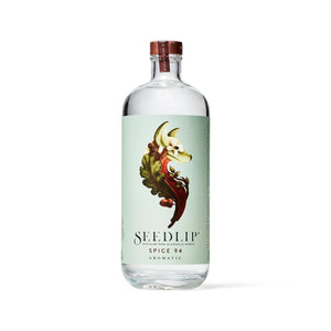A clear bottle of SEEDLIP - SPICE 94 NON ALCOHOLIC SPIRIT by SEEDLIP DRINKS, featuring a light green label with leaves and spices, plus a copper-colored cap, displayed against a white background.