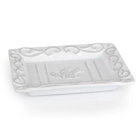 Introducing the CERAMIC SOAP DISH by EUROPEAN SOAPS, LLC: a small, rectangular white ceramic dish adorned with ornate, raised scroll designs around the edges. The center showcases a bird in flight carrying a branch in its beak, making this elegant piece reminiscent of white-washed ceramics and perfect for gift occasions.