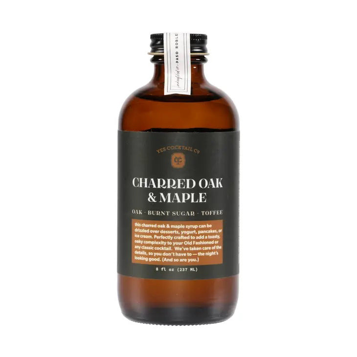 A brown glass bottle with a black label reading "YES COCKTAIL CO - CHARRED OAK &amp; MAPLE" features ingredients like oak, burnt sugar, and toffee. The small text describes the product as an ideal maple syrup for classic cocktails. The bottle size is 8 fl oz (237 ml).