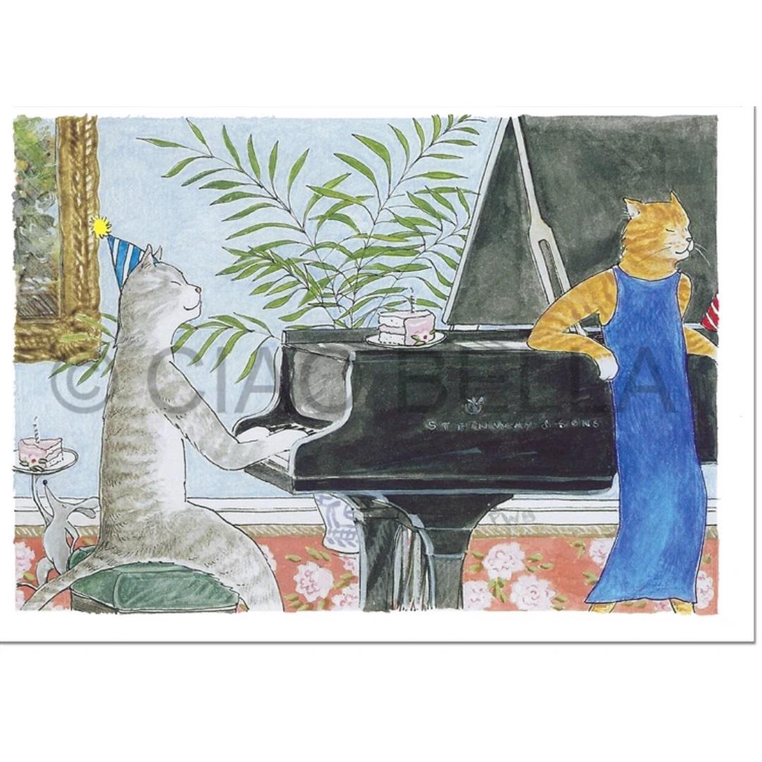 The CIAO BELLA - SATIN DOLL CARD by CIAO BELLA features a vivid illustration of two cats at a musical party. One cat, wearing a party hat, sits on a stool playing a grand piano while the other cat, dressed in a blue dress, stands beside it. The scene is completed with potted plants and a floral-patterned carpet in the background.
