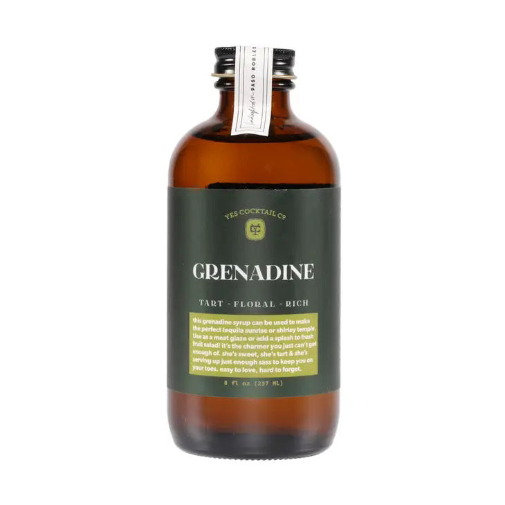 A brown glass bottle with a black label from YES Cocktail Co. contains YES COCKTAIL CO - GRENADINE, making it ideal for classic cocktails like a Tequila Sunrise. The label prominently displays &quot;GRENADINE&quot; in bold, accompanied by the descriptors &quot;Tart - Floral - Rich&quot; underneath. It features a black screw cap and holds 8 fl oz (237 ml).