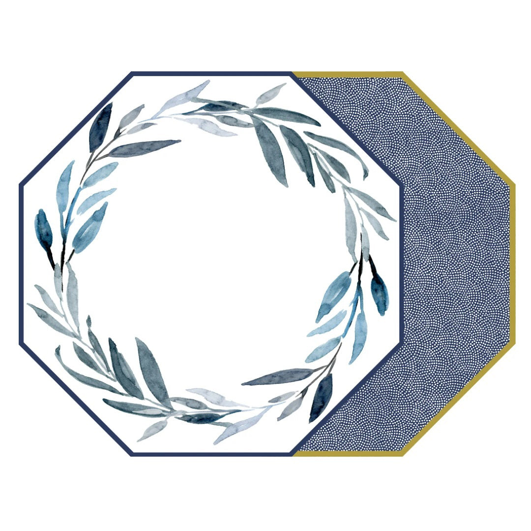 The HOLLY STUART DESIGNS - WATERCOLOR LEAVES PLACEMAT by HOLLY STUART DESIGNS is octagon-shaped and double-sided. The front showcases a wreath of green and blue leaves on a white background with a polyurethane protective coating, while the back side features a dark blue and white polka dot texture, bordered by a yellow stripe.