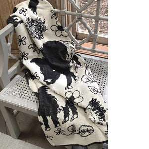 Presenting the FEARRINGTON SIGNATURE COLLECTION - BELTIE BARNYARD KNIT THROW by CALHOUN & CO., this cylindrical knitted item showcases a black and white design with a close-up of a rabbit holding a flower. Made in America, it features minimal detailing that emphasizes contrasting shades, creating a simple and stylized depiction of the rabbit and flower.