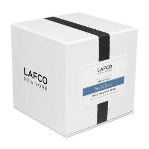 The LAFCO - SEA DUNE, BEACH HOUSE 6.5oz votive candle holder is displayed against a plain white background. Featuring a clear cylindrical design with a white inner surface, this sleek and minimalistic piece evokes the tranquil decor of a beach house, casting a subtle shadow to the right.