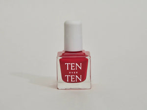 A glass bottle of TENOVERTEN - NAIL POLISH from the brand TEN OVER TEN, featuring a white cap and a dusty pink nail color. The front label displays "TEN OVER TEN" in white uppercase letters. This vegan, eight-free formula ensures both beauty and peace of mind. The background is plain and light-colored.