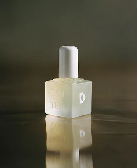A bottle of TENOVERTEN - THE REHAB BASE COAT with a white cap is placed next to a light green box featuring the brand name 'TEN OVER TEN' and product details, perfect for those seeking to maintain nail health. The background is a textured, reflective surface.