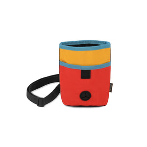 The TREAT POUCH SUNRISE from PLAY PET LIFESTYLE is a color-blocked rectangular deluxe treat pouch with a top zipper. This multi-functional dog accessory features a bright red bottom section, a yellow middle section, and a blue top section. It has a black adjustable strap and displays a small black round patch with an embroidered symbol on the front.