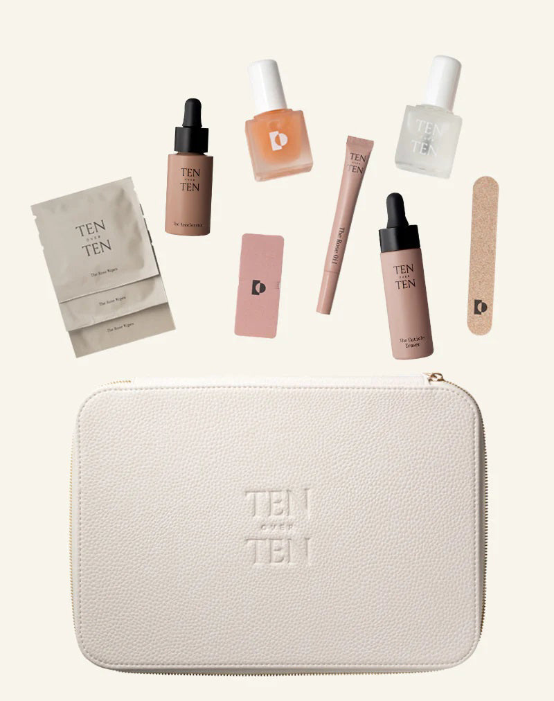 The TENOVERTEN - THE MANICURE KIT, by TEN OVER TEN, is showcased alongside various cosmetic items. The beige pouch features the text "TEN OUT OF TEN" and includes a Rose Oil dropper bottle, The Foundation, a cuticle eraser, a nail file, clear and white nail polish, a square bottle, a small box, and a tube.